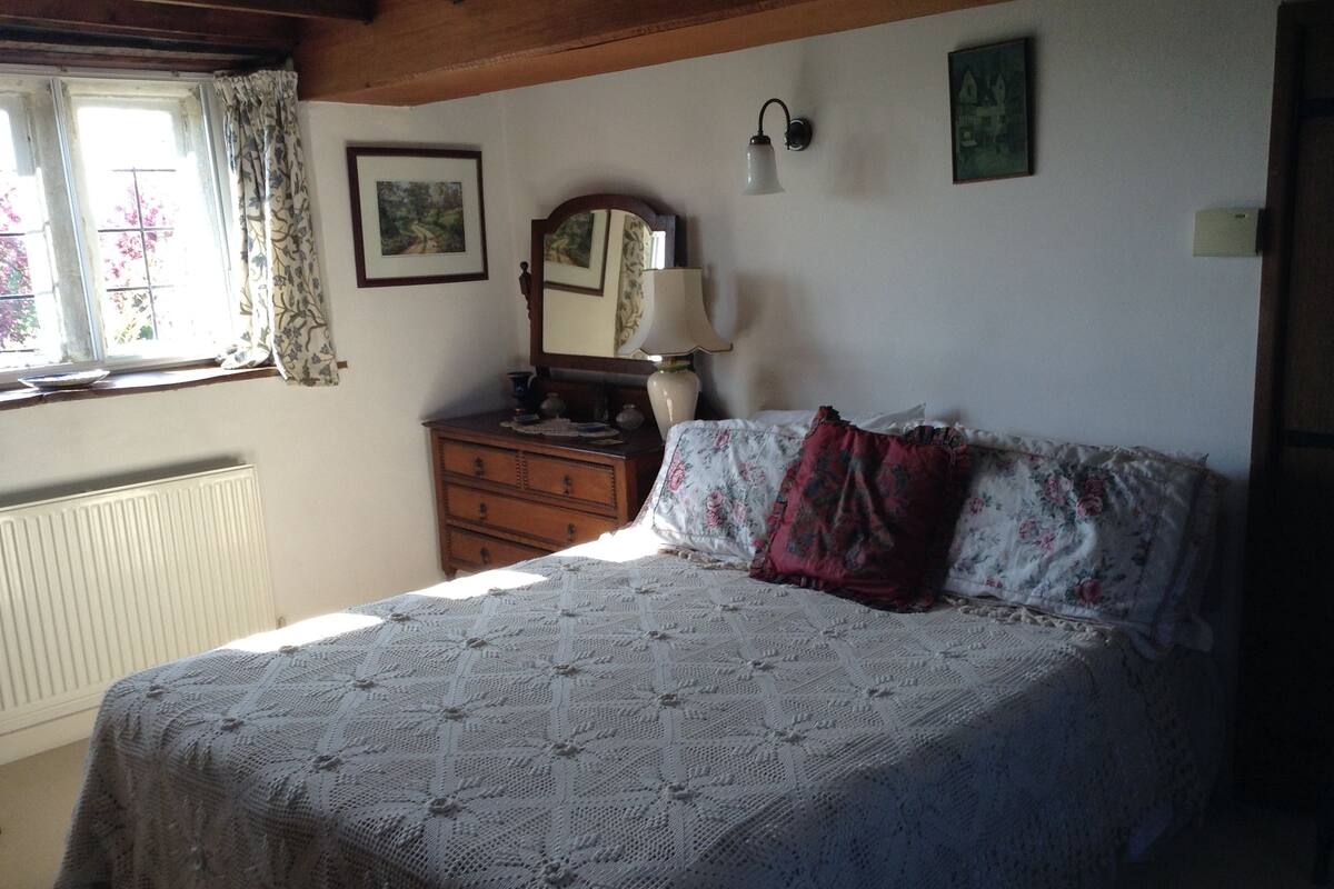 A bedroom with a bed, dresser, and a window with curtains.