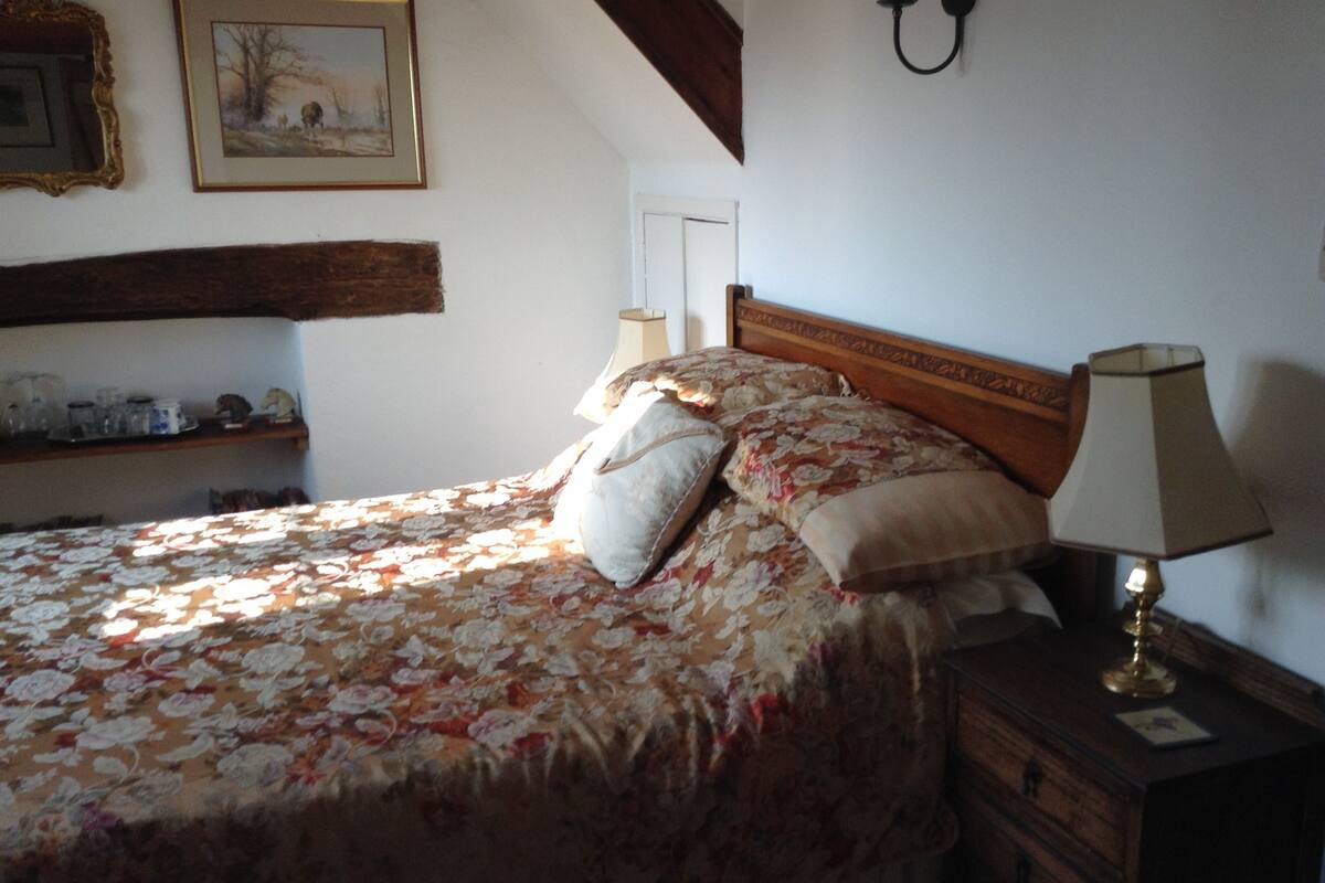 A bedroom with a floral bedspread, a wooden headboard, a bedside lamp, and a framed picture on the wall.