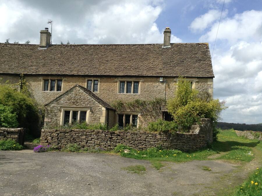 A stone house with a tiled roof, multiple windows, and a stone wall surrounding the property.