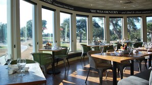 Un restaurante con grandes ventanales, sillas de mimbre y mesas dispuestas para comer.