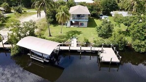 Een huis met een groot terras dat uitsteekt over het water, omgeven door weelderige begroeiing en palmbomen.