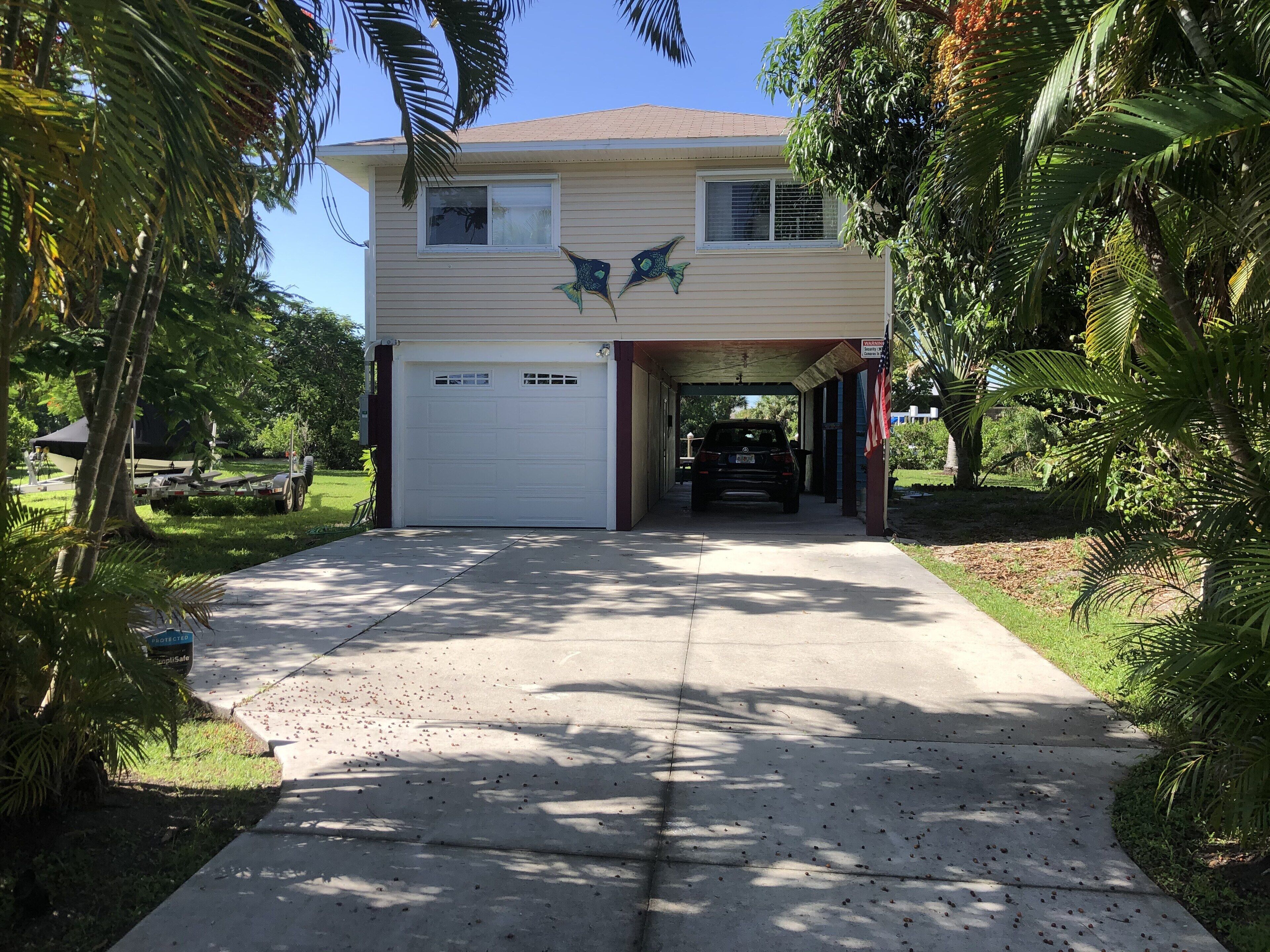 A two-story house with a garage, surrounded by palm trees and a clear sky.