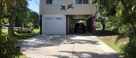 A two-story house with a garage, surrounded by palm trees and a clear sky.