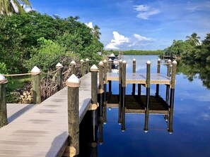 A wooden dock with rope railings leading to a pier over calm water, surrounded by lush greenery. - Stunning Nature! Waterfront! Prime Fishing! Bring Boat. Free Bikes, SUP, Kayak. (Bokeelia)