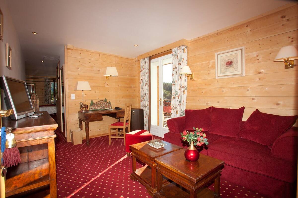 Une pièce chaleureuse avec un décor intérieur en bois, un canapé rouge, un bureau en bois avec une lampe et un téléviseur posé sur un meuble en bois.