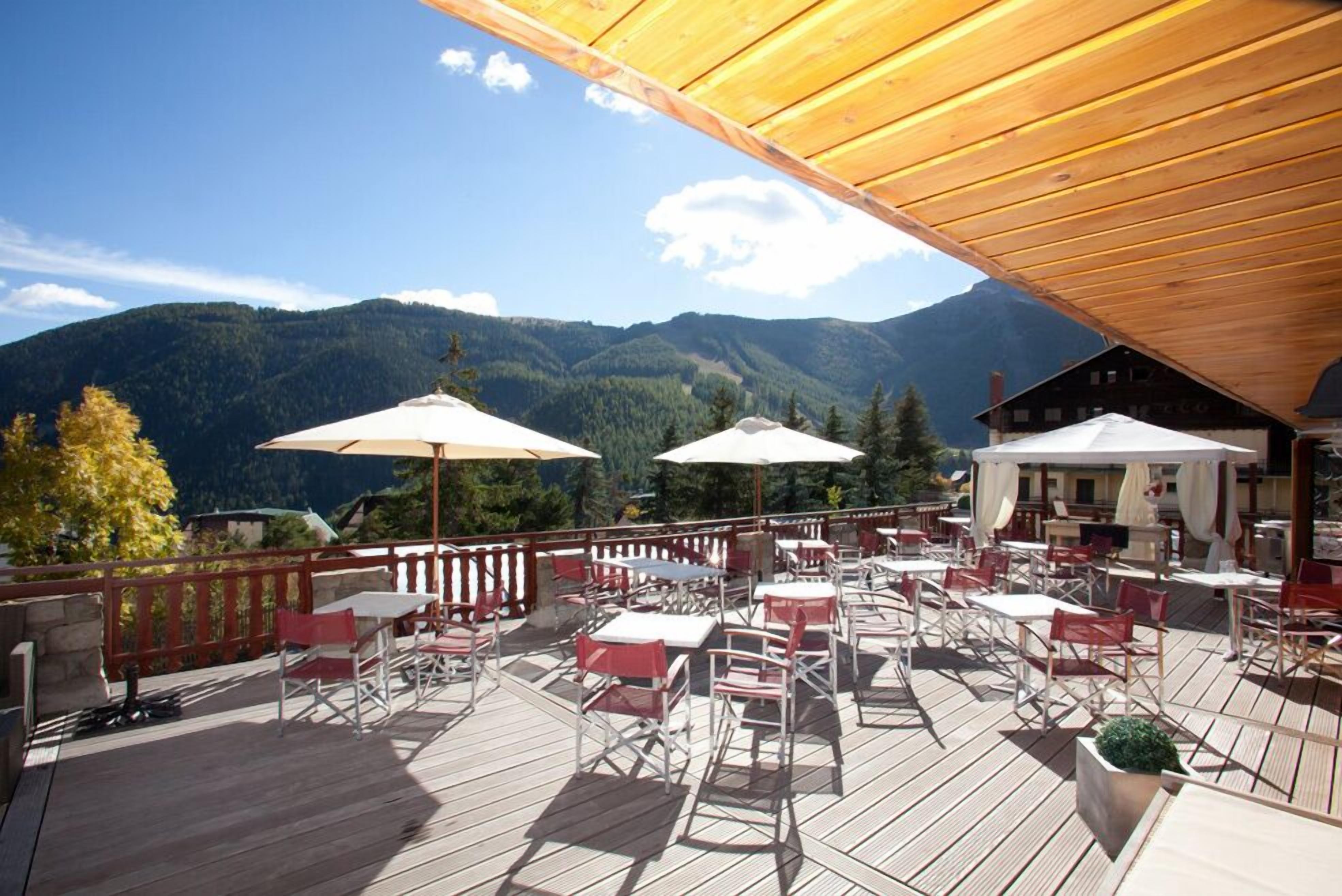 Eine Holzterrasse mit Außenmöbeln und Tischen, mit Blick auf eine gebirgige Landschaft.