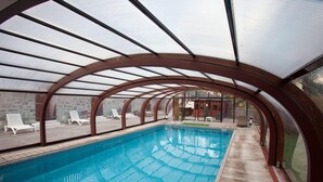 An indoor swimming pool with a wooden deck and lounge chairs, enclosed by a glass and metal structure. - Le Chalet d'Auron (Saint-Etienne-de-Tinee)