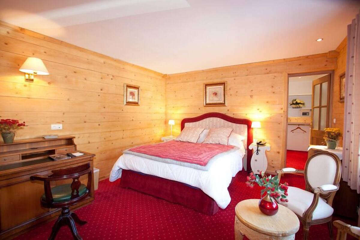 Une chambre à coucher aux murs lambrissés, comprenant un lit, des tables de chevet, un bureau et une chaise.