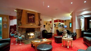 A hotel lobby with a stone fireplace, leather sofas, a wooden coffee table, and a red carpeted floor. - Le Chalet d'Auron (Saint-Etienne-de-Tinee)