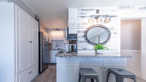 A kitchen with white cabinetry, a granite countertop, a stainless steel refrigerator, and a large mirror above the sink. - The Summit 1BR 1.5BA Beautiful unit with great views! (Panama City Beach)