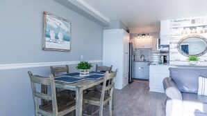 A dining area with a wooden table and chairs, a framed painting on the wall, and a kitchen in the background. - The Summit 1BR 1.5BA Beautiful unit with great views! (Panama City Beach)