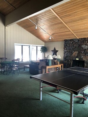 A room with a ping pong table, a stone fireplace, and a large window. - SV121 - Walk to Lifts & Town - Hot Tub & Pool (Ketchum)