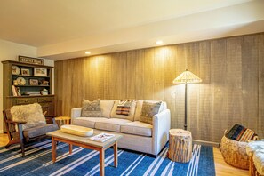 Ein Wohnzimmer mit einer Couch, einem Couchtisch und einer Lampe. Ein Bücherregal zeigt verschiedene Gegenstände.