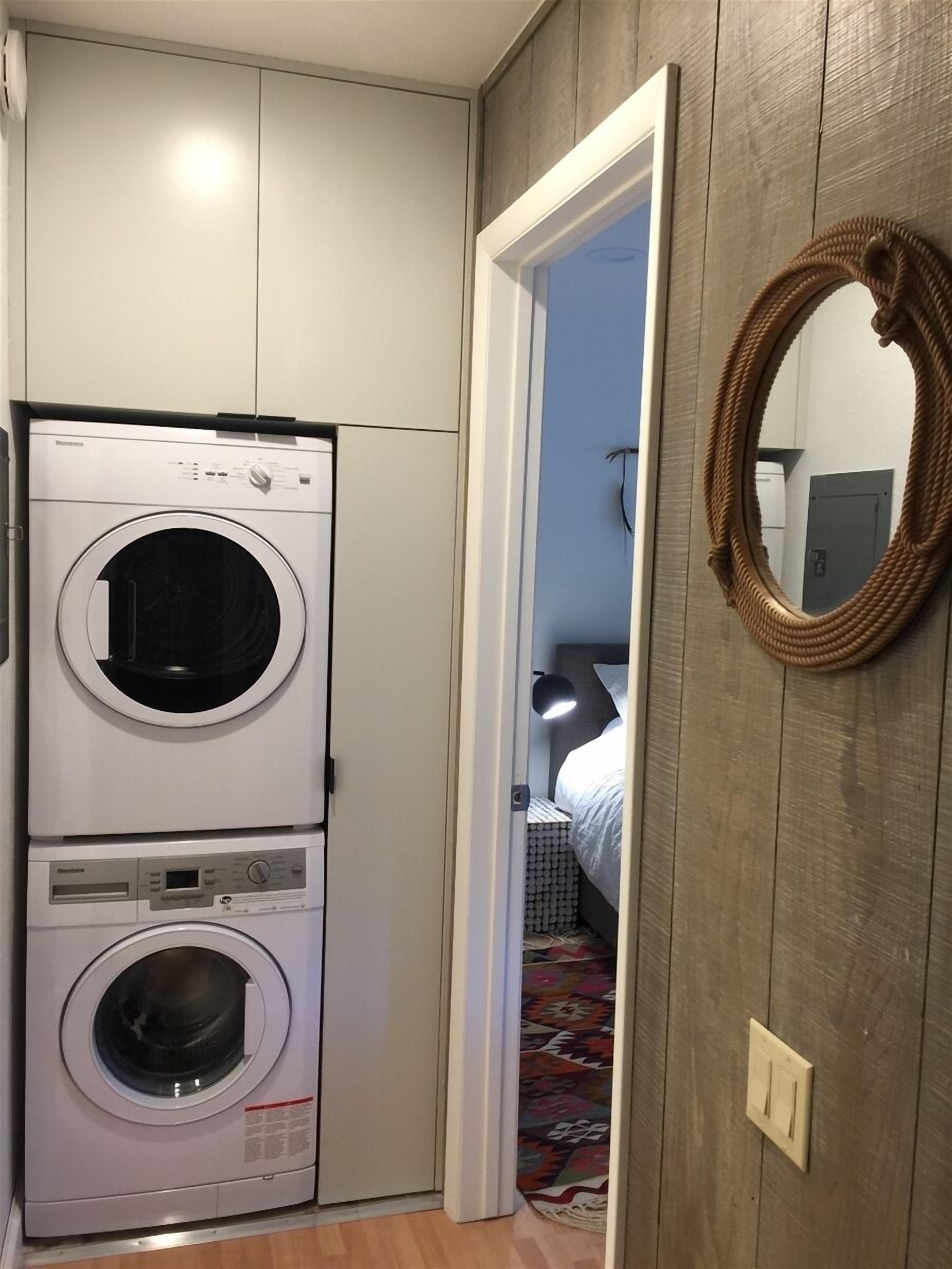 A compact laundry room with stacked washing machines, a wooden wall, and a mirror.