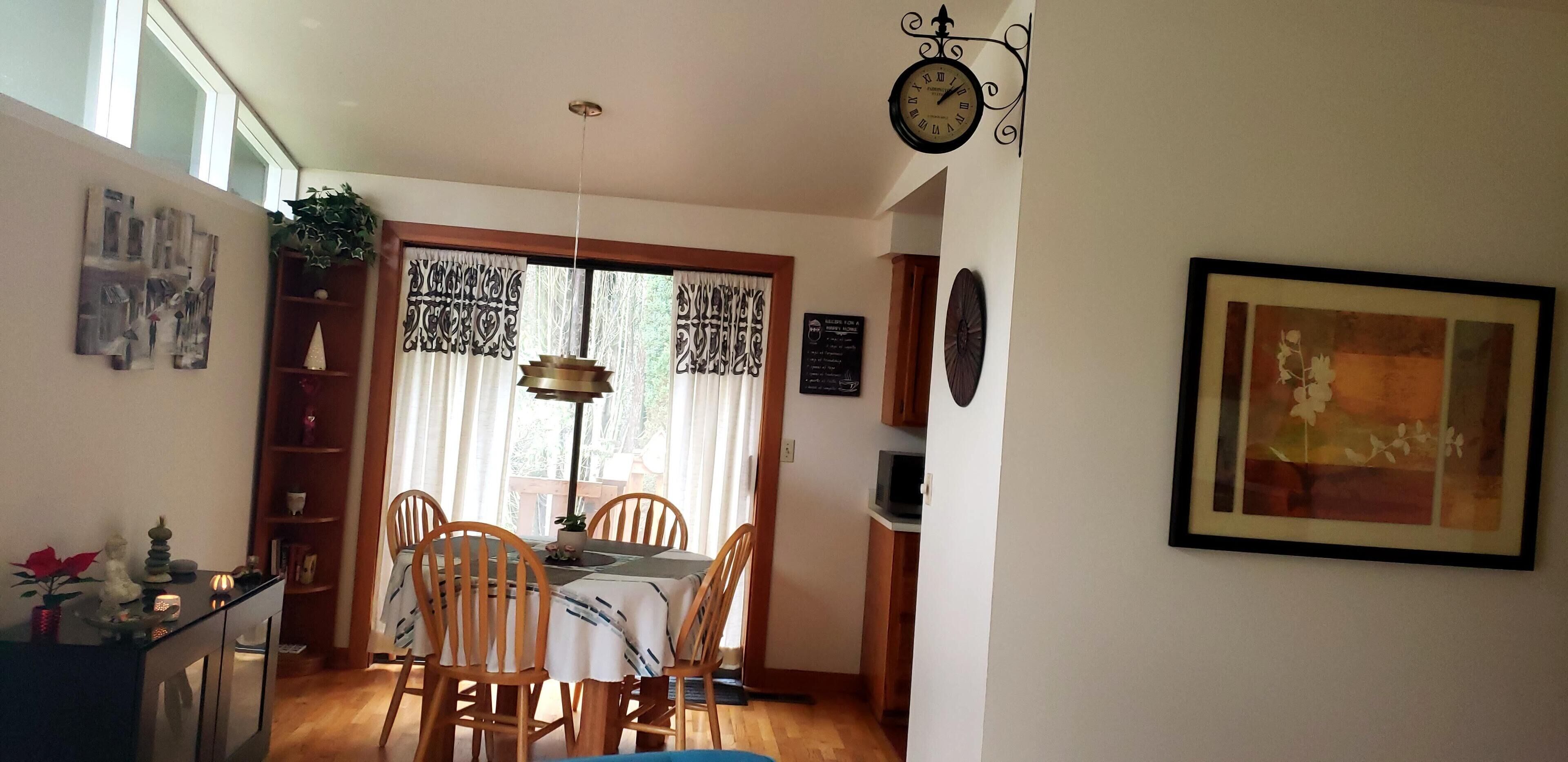 A dining area with a table and chairs, a clock, and a framed picture on the wall.