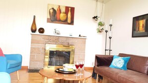 A living room with a fireplace, blue and brown sofas, a coffee table with a tray and glasses, and wall art. - Beautiful Home with Traditional & Modern Ambience (Edmonds)