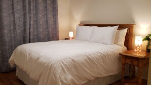 A neatly made bed with white linens, a wooden headboard, and a bedside table with a lamp and a small plant. - Beautiful Home with Traditional & Modern Ambience (Edmonds)