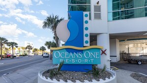 Un letrero para Oceans One Resort con un diseño estilizado de ola y un símbolo de ancla roja.