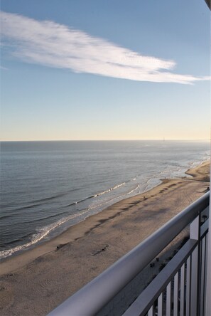 A beach view from a balcony with a railing, ocean waves, and a clear sky.