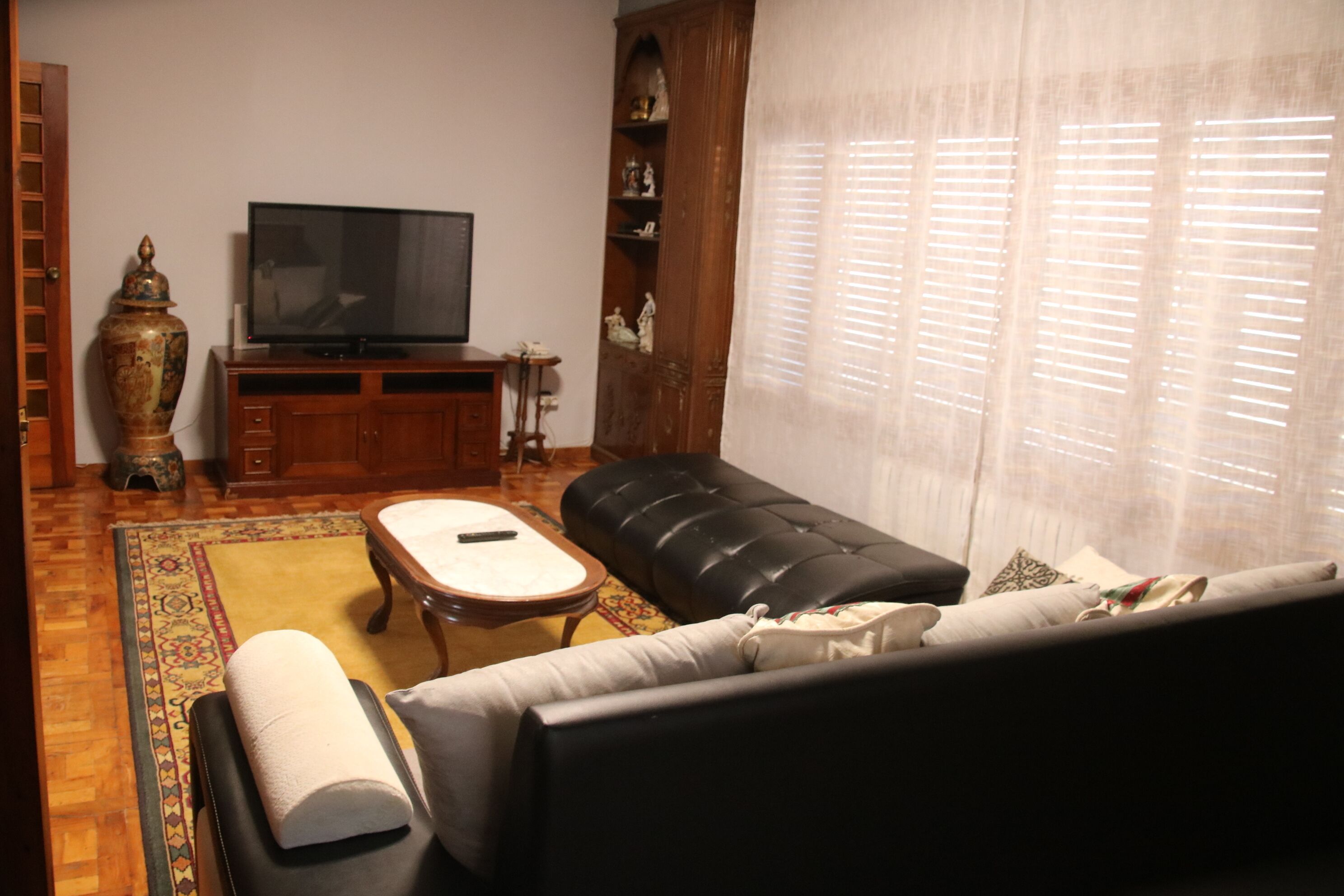 Una sala de estar con sofá, otoman, mesa de centro, televisor, aparador de madera y un jarrón grande.
