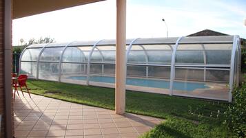 Un patio cubierto con una estructura tipo invernadero de vidrio, una piscina y piso de baldosas.