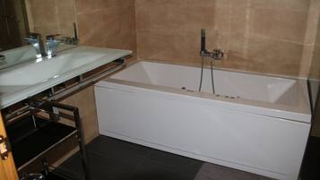 Un baño con una bañera blanca, un tocador de vidrio y una zona de ducha.