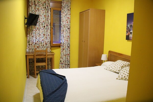 A room with a bed, a desk, a chair, a wardrobe, and a television. - Hostal Burgalés (Milagro)