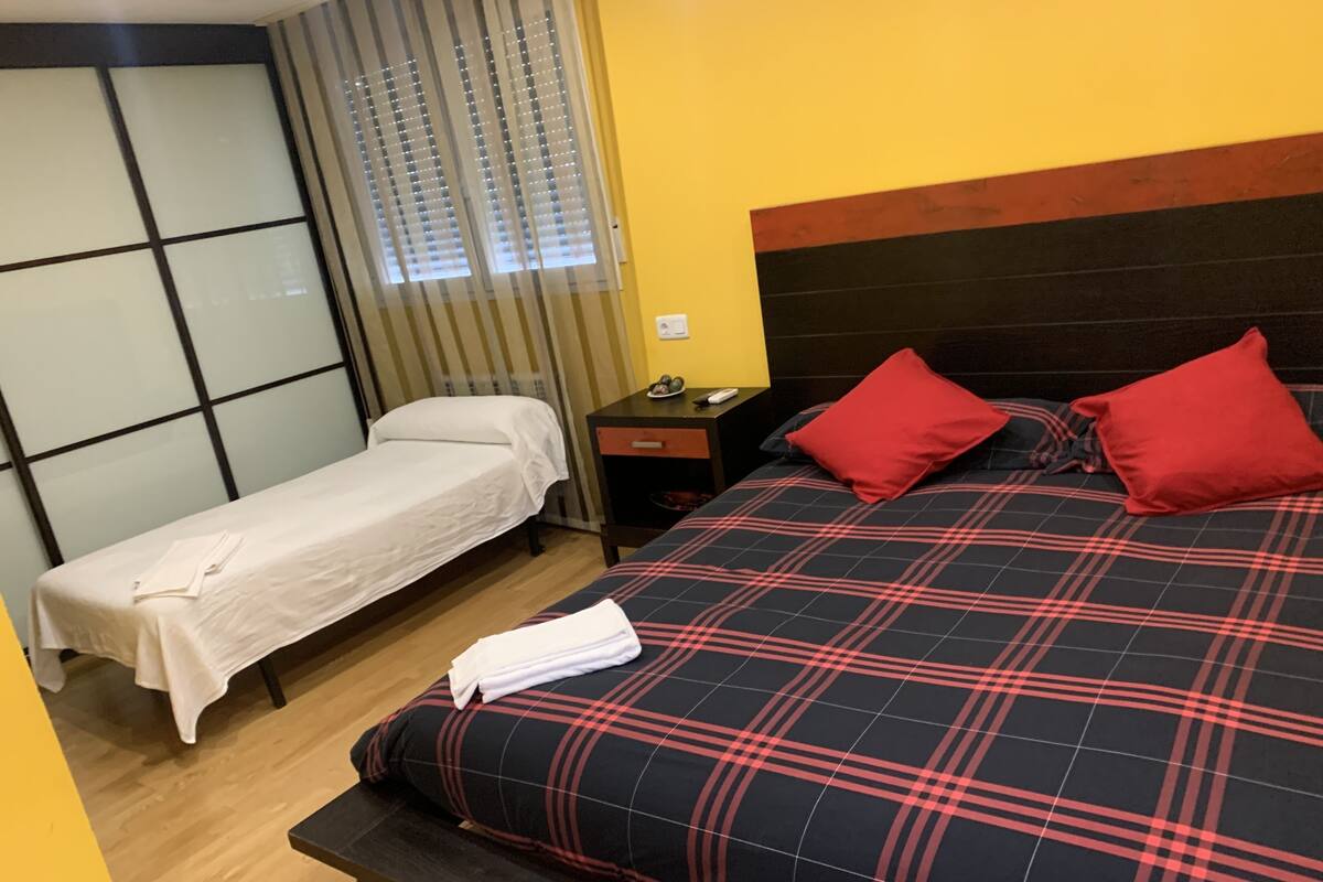 Ein Hotelzimmer mit einem Bett, einem Einzelbett, einem Nachttisch und einem Fenster mit Jalousien.