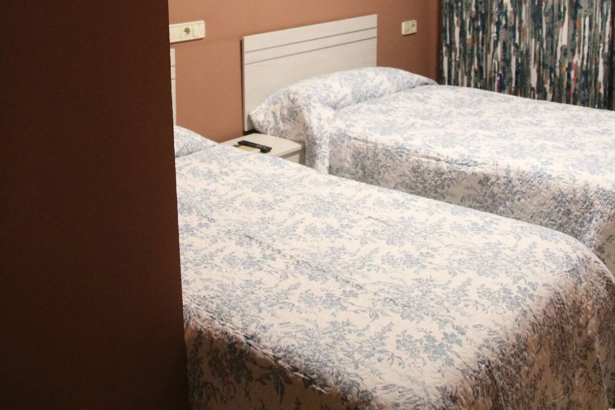 Ein Hotelzimmer mit zwei Einzelbetten, einem Kopfteil, einem Wandbild und einem Vorhang.