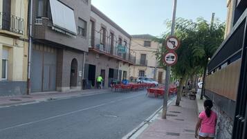 A street with a sidewalk, a pedestrian, and a row of outdoor tables and chairs.