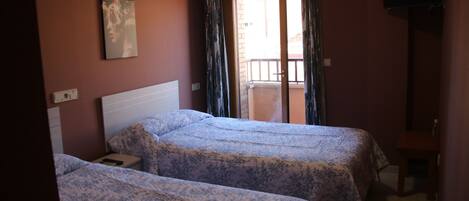 A room with two beds, a TV on the wall, and a balcony with curtains.