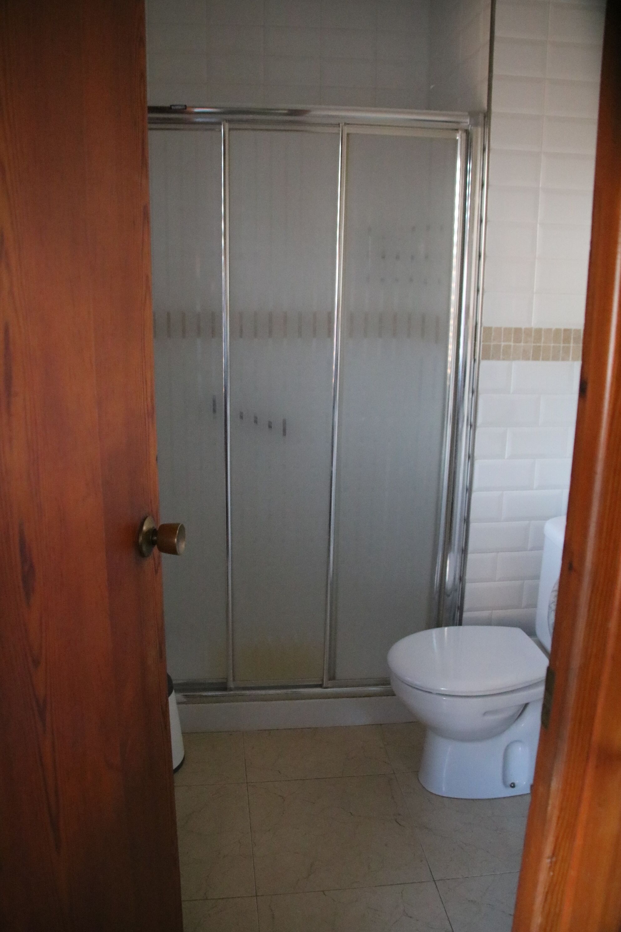 Baño con cabina de ducha, inodoro y piso de baldosas.