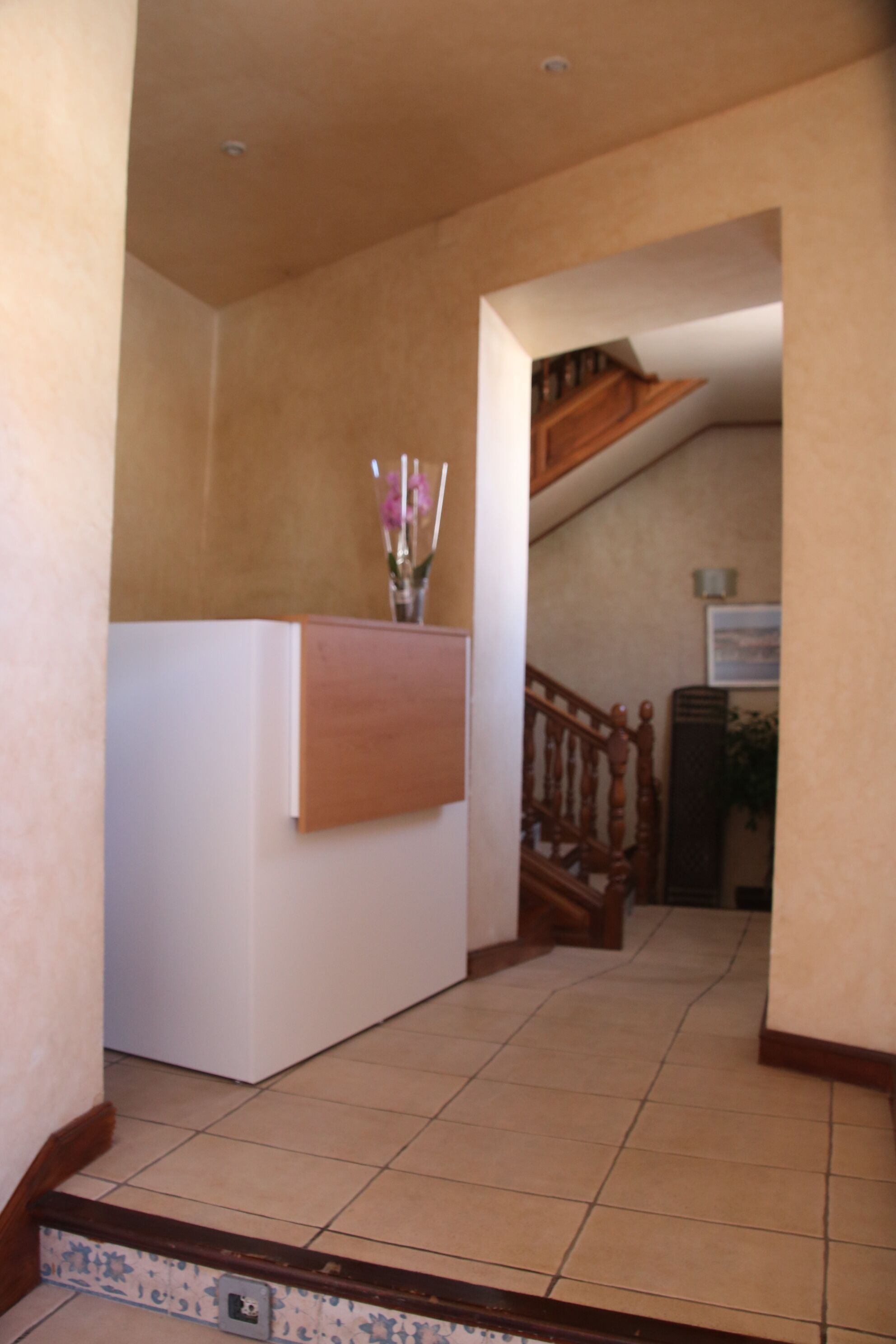 Un pasillo con mostrador de recepción, escalera de madera y suelo de baldosas.