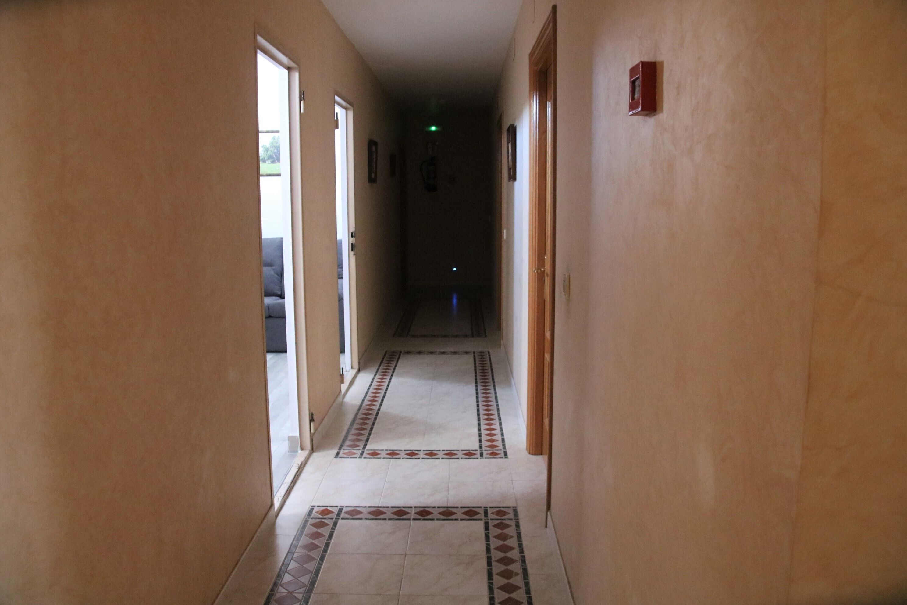 Un pasillo con paredes color beige y baldosas de suelo estampadas, que conduce a una habitación oscura al final.