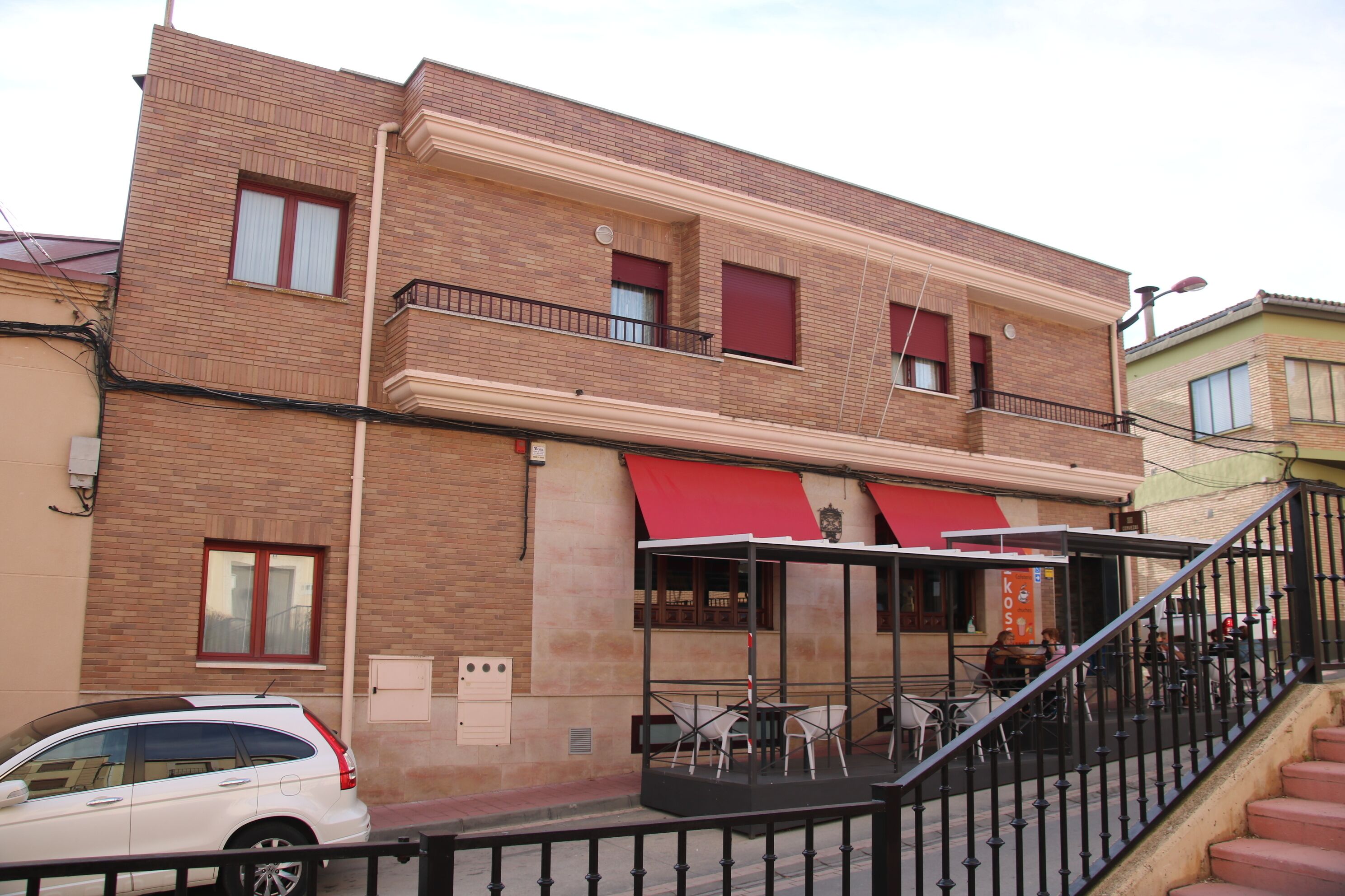 Un edificio de dos pisos con toldo rojo y zona de estar al aire libre.