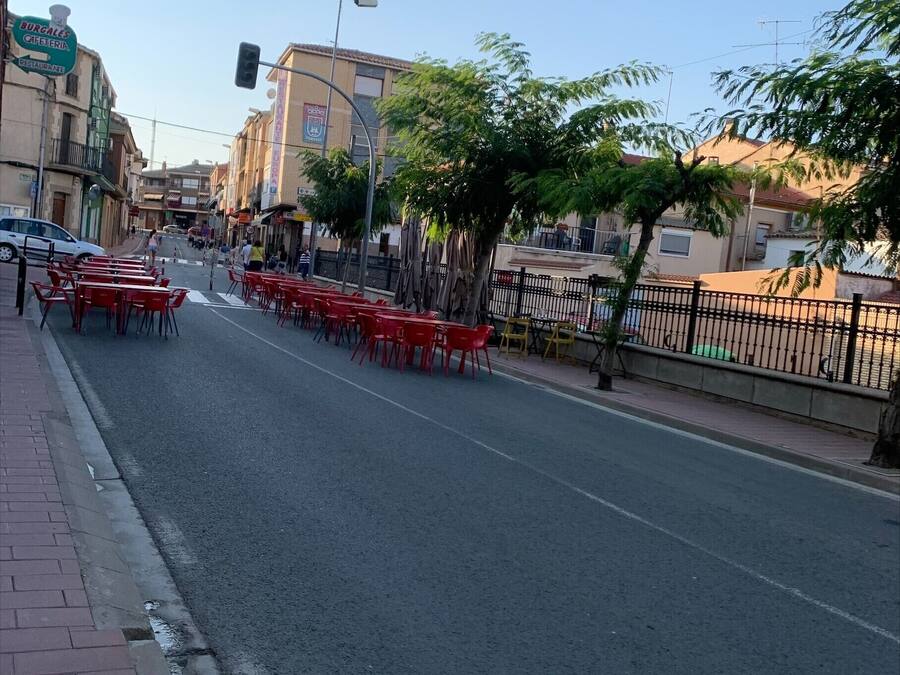Uma rua com cadeiras vermelhas dispostas de um lado, céu claro e edifícios ao fundo.