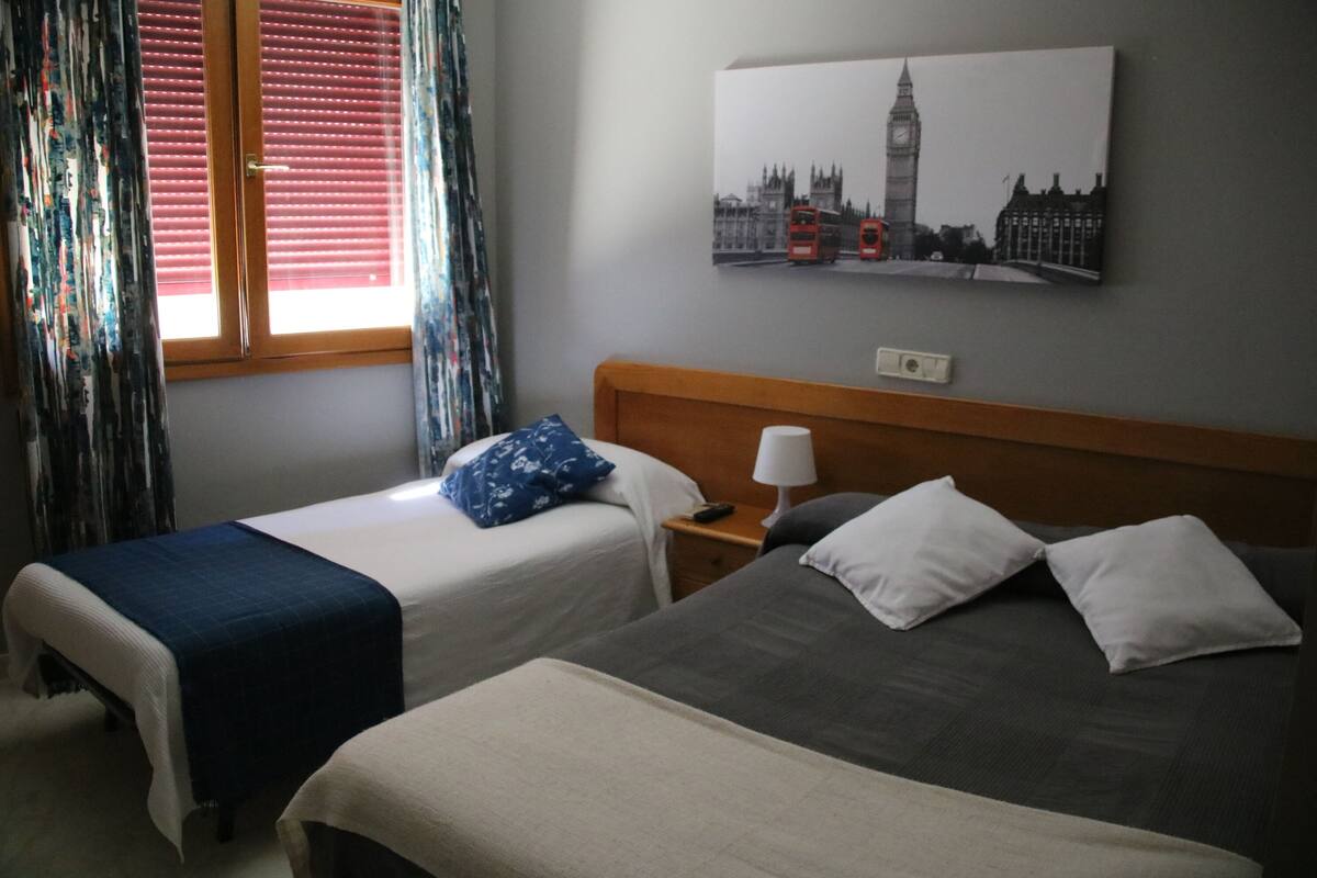 Ein Hotelzimmer mit zwei Betten, einem Nachttisch, einer Lampe und einem Fenster mit Vorhängen.