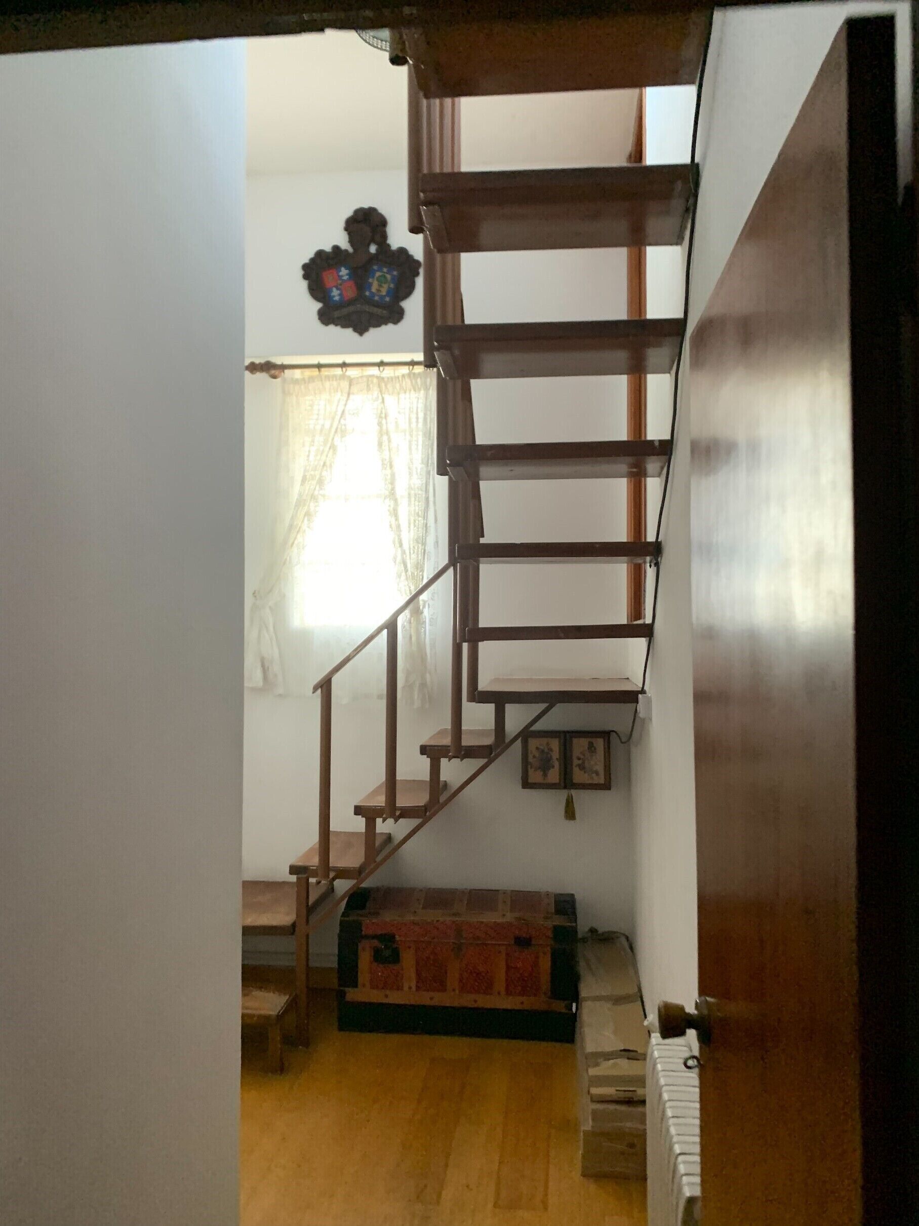 A wooden staircase leading to a second floor, a radiator, and a window with sheer curtains.