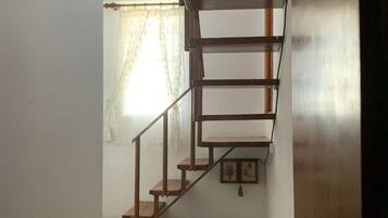 A wooden staircase leading to a second floor, a radiator, and a window with sheer curtains.
