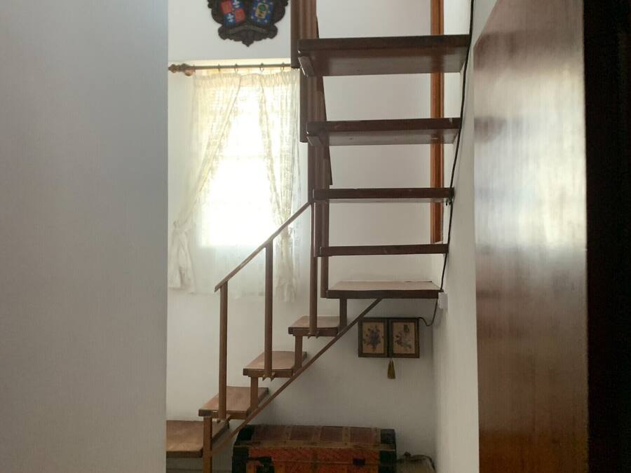 A wooden staircase leading to a second floor, a radiator, and a window with sheer curtains.