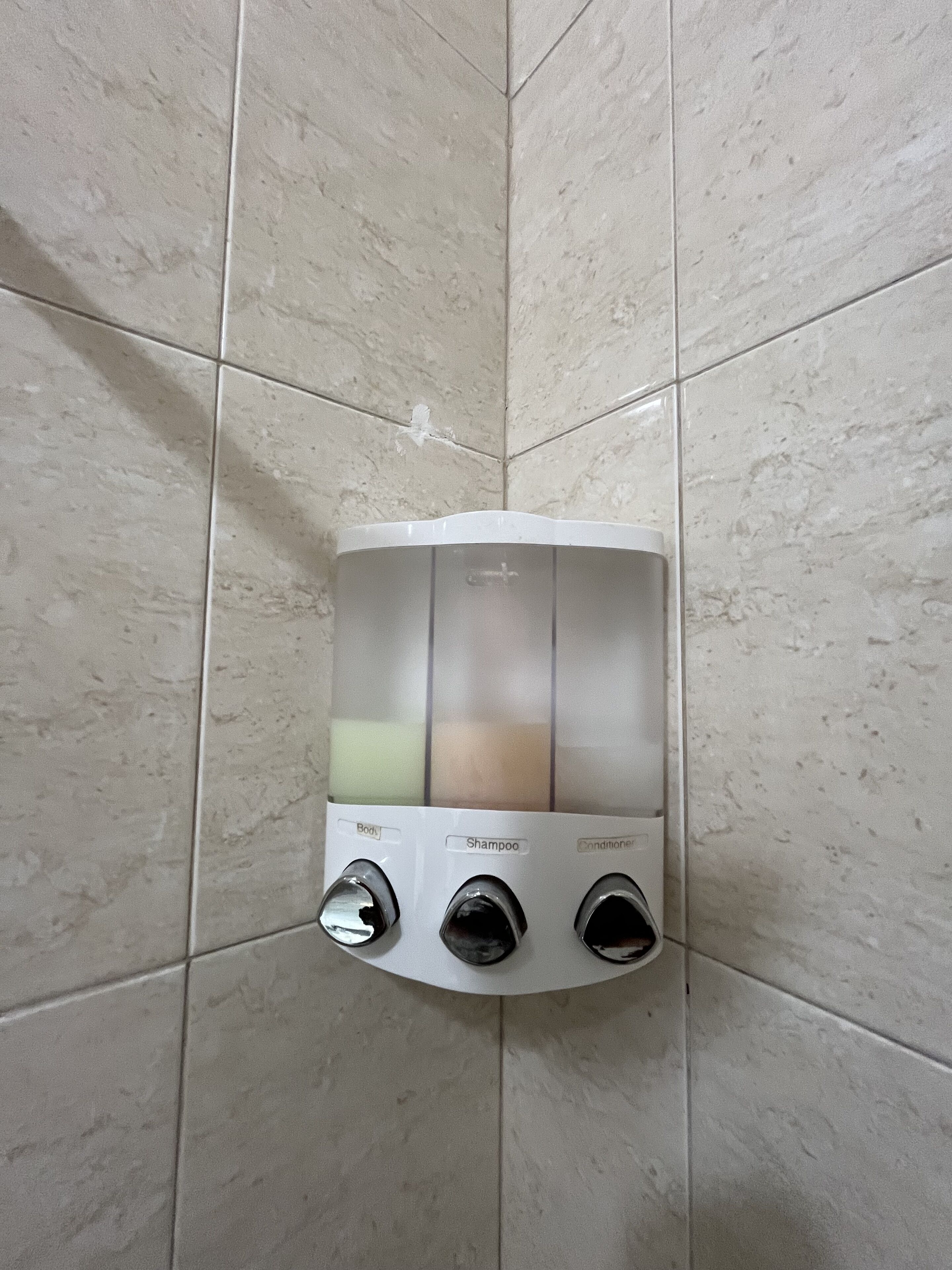 A wall-mounted dispenser with three outlets labeled "Body," "Shampoo," and "Conditioner."