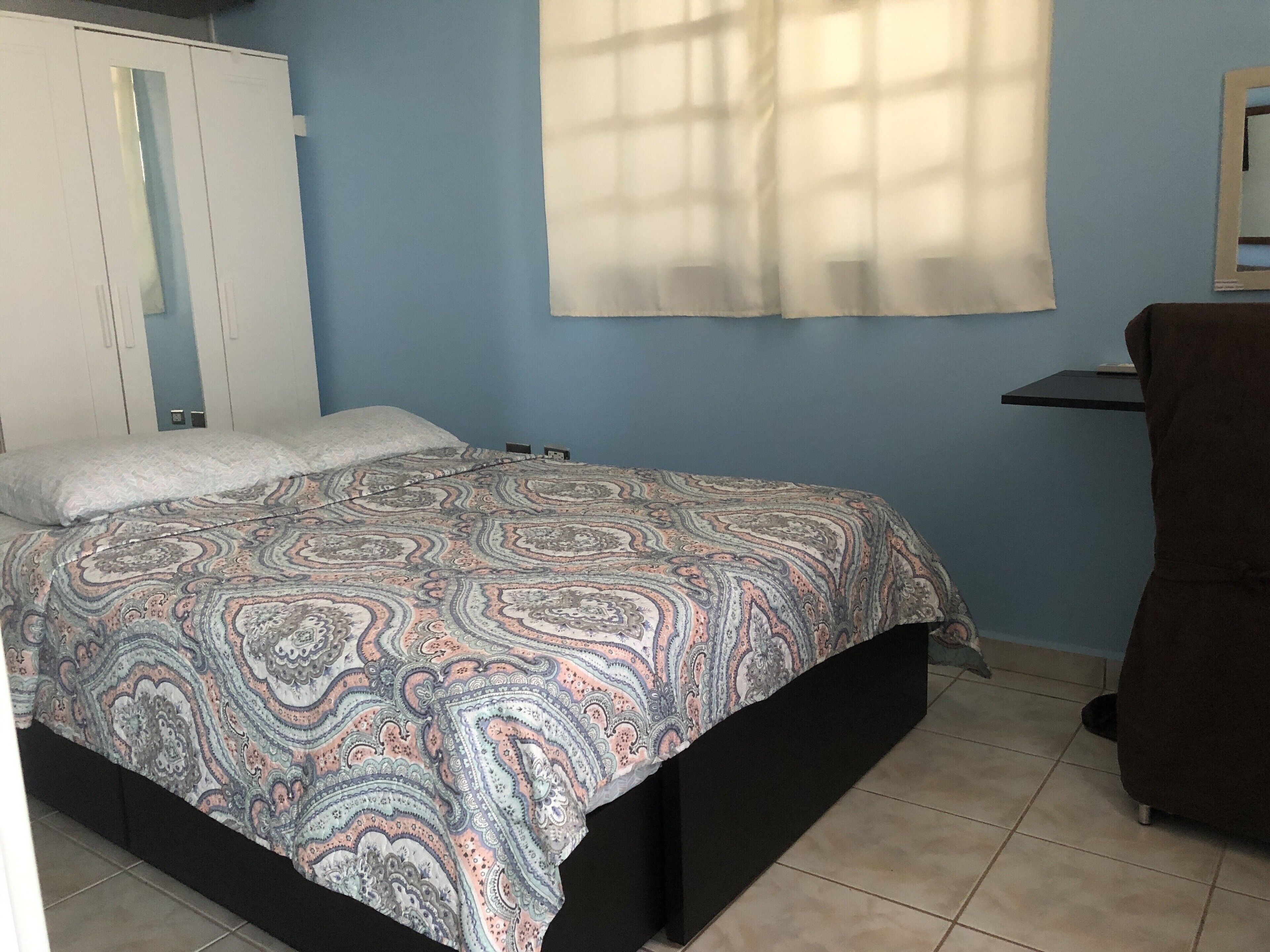 Une chambre à coucher avec un lit, une armoire, une fenêtre avec des rideaux et une petite table.