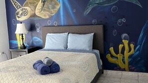 Et soveværelse med seng, natbord, lampe og et vægmaleri af havdyr.