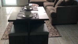 En stue med sofa, sofabord og spisebord dækket med tallerkener og bestik.