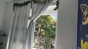 Et værelse med seng, tv og udsigt til en balkon med gelænder og grøn bevoksning.