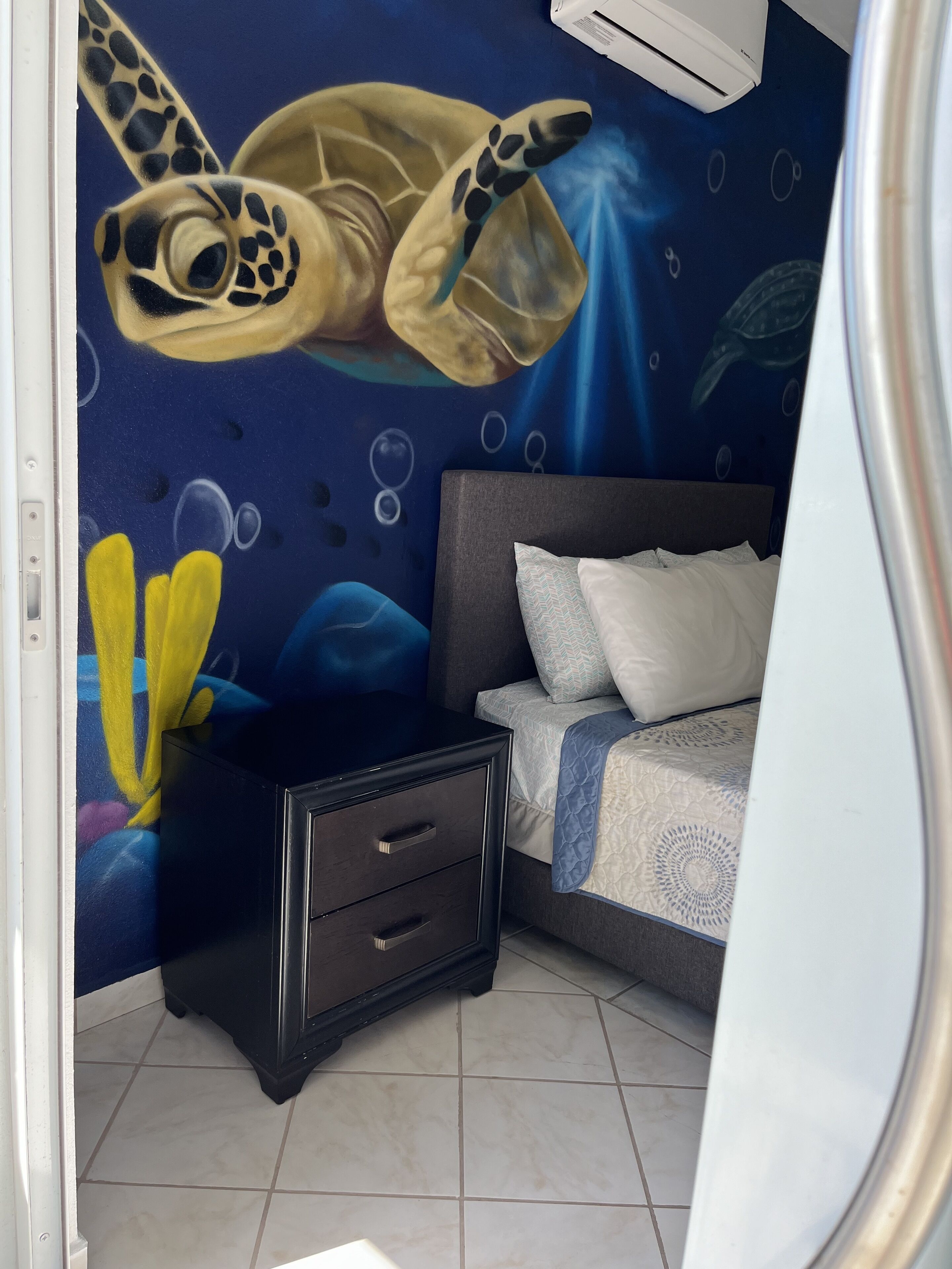 A bedroom with a bed, a dresser, and a mural of sea turtles on the wall.