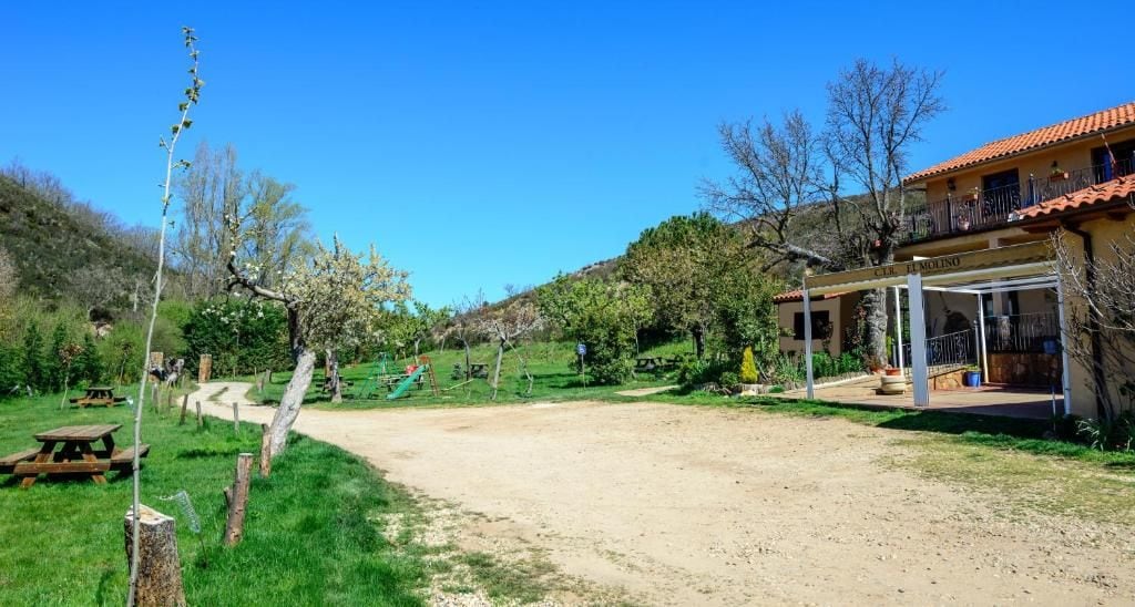 Una propiedad rural con camino de tierra, mesas de picnic y un espacio de estar al aire libre cubierto.