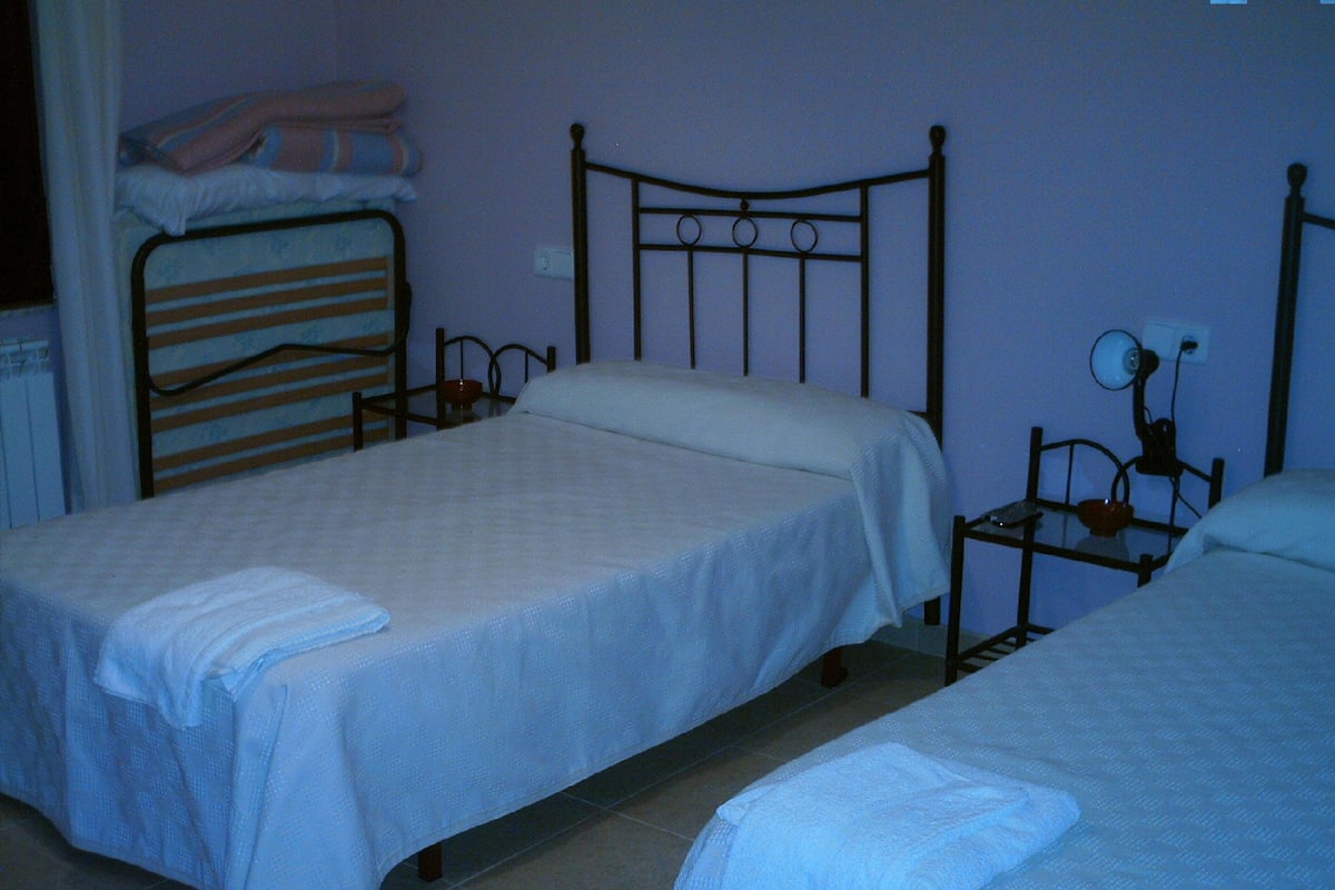 Ein Zimmer mit zwei Einzelbetten, einem kleinen Tisch mit Lampe und einem Heizkörper.