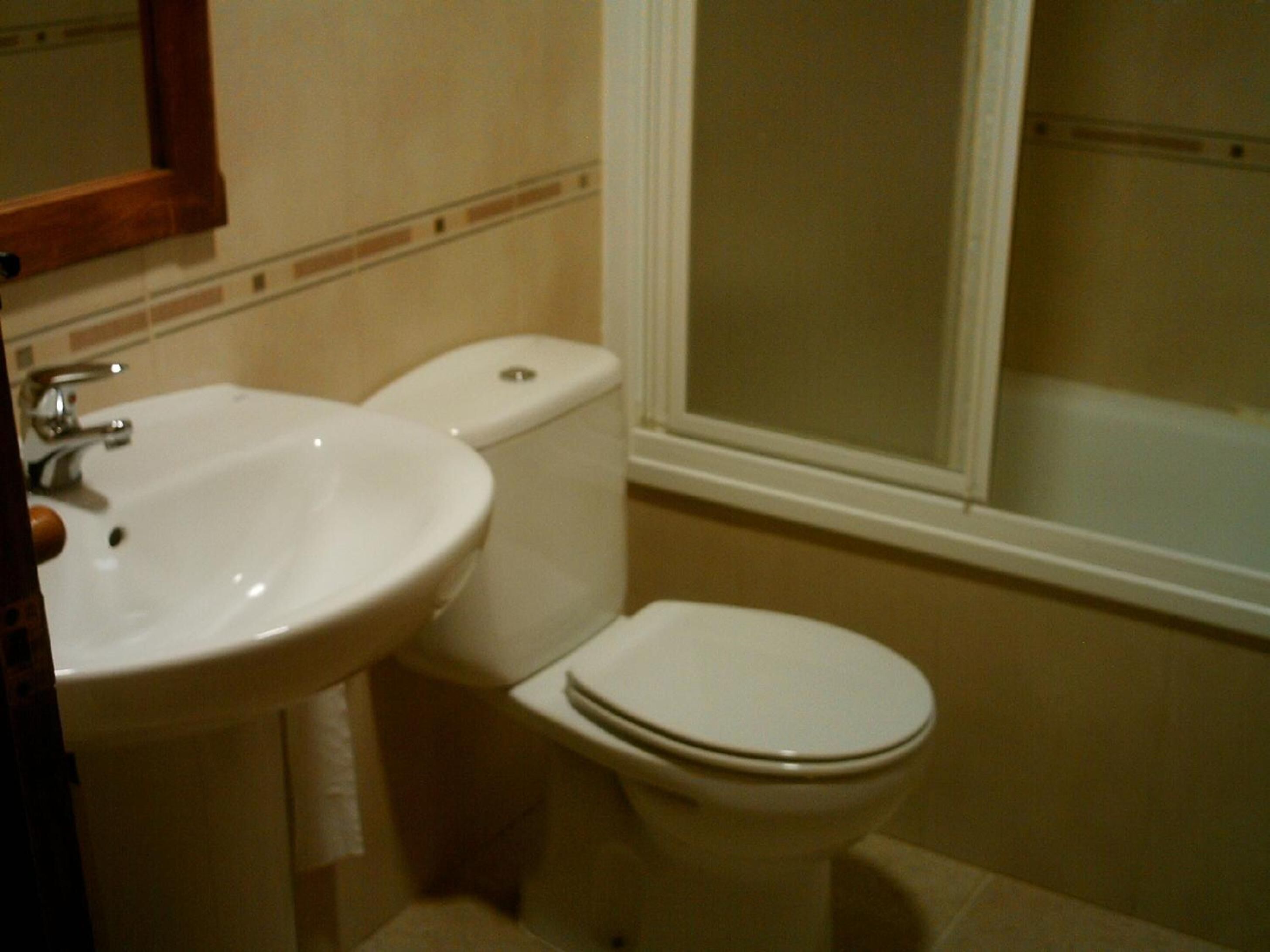 Un baño con lavamanos blanco, inodoro y ventana con vistas a un edificio.