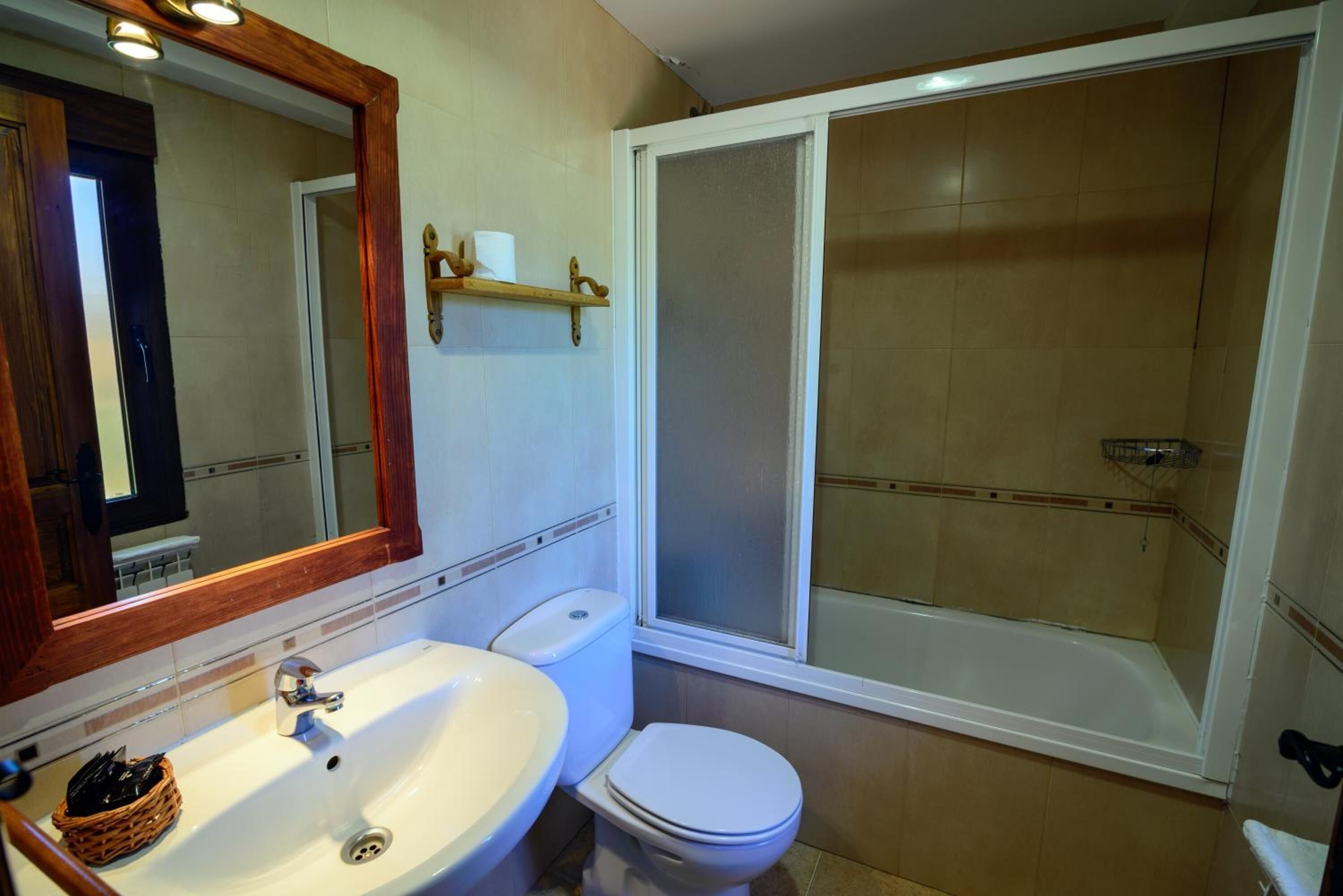 Un baño con lavamanos blanco, inodoro y ducha a ras de suelo con puerta de vidrio.